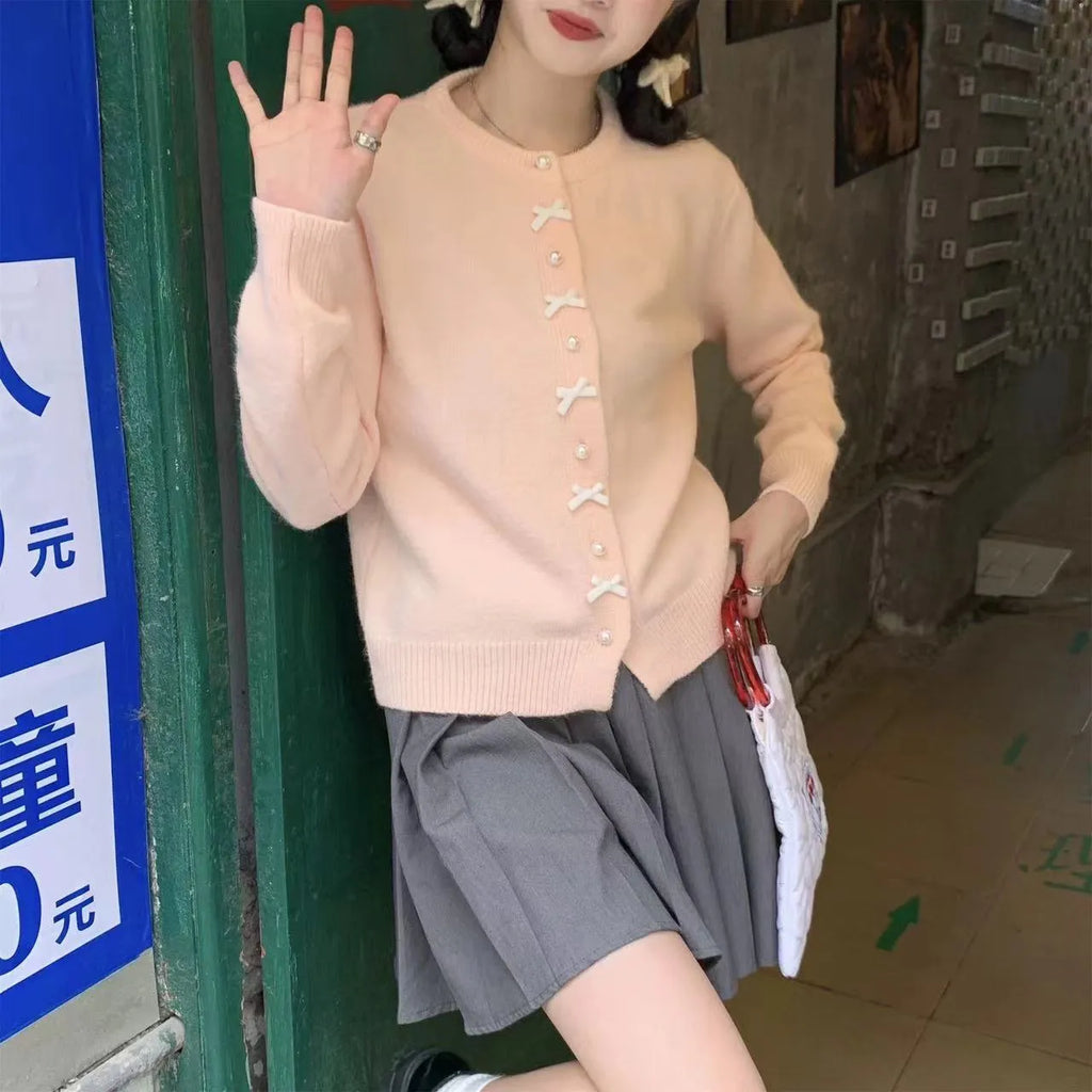 Women's solid colour cardigan with a front fabric bow and pearl button fastening, shown in a light colour.