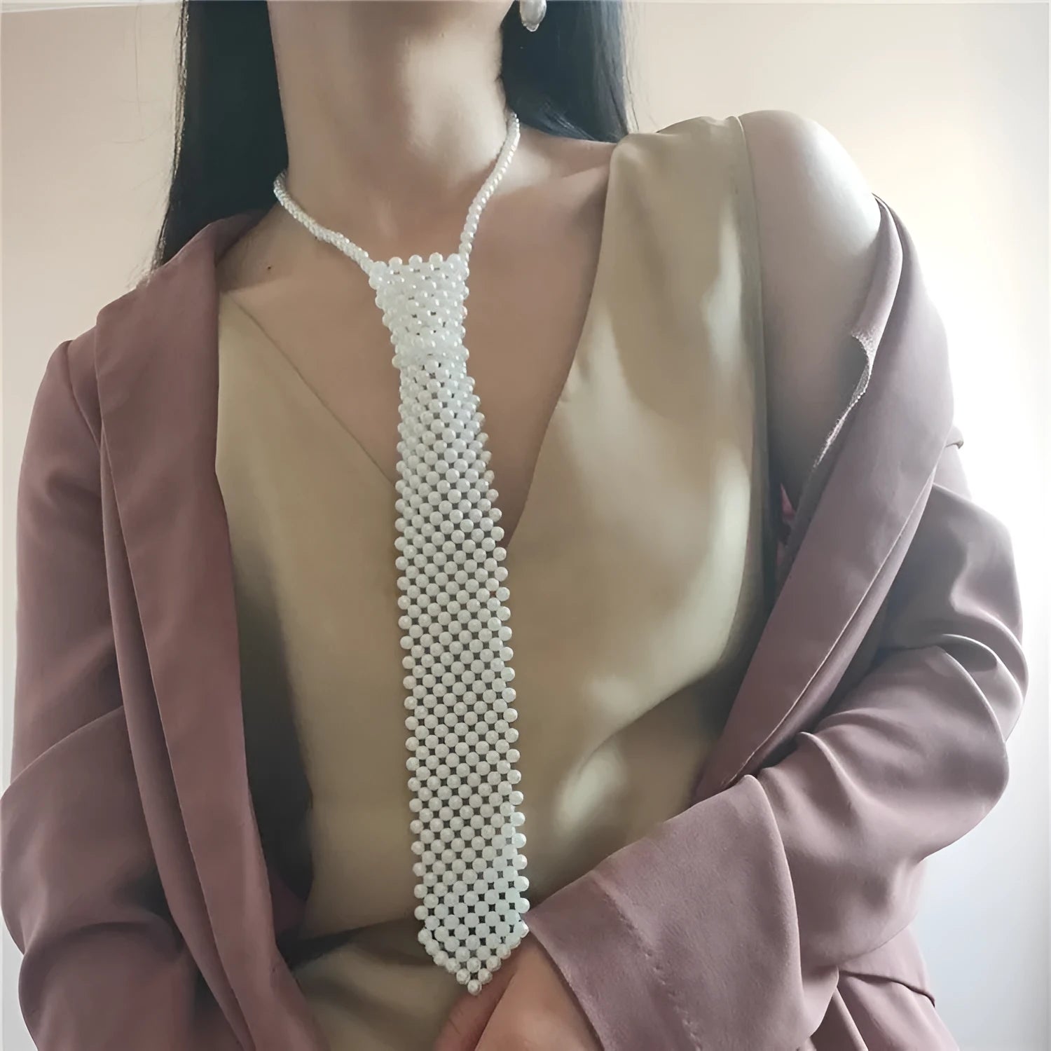 Close-up of a white imitation pearl body chain with an adjustable alloy tie clasp on a dark background.