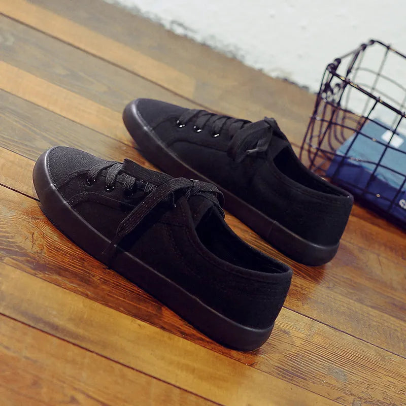 All black low-top canvas lace-up flat shoes for women with a rubber sole.