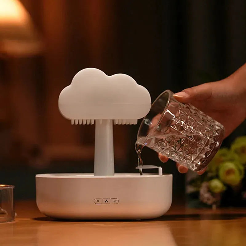 White cloud-shaped humidifier diffuser with multi-colour LED lights on a wooden surface.