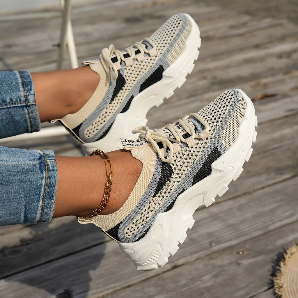 Women's Flyknit mesh sneakers in grey and white, showcasing the breathable upper and flat rubber sole.