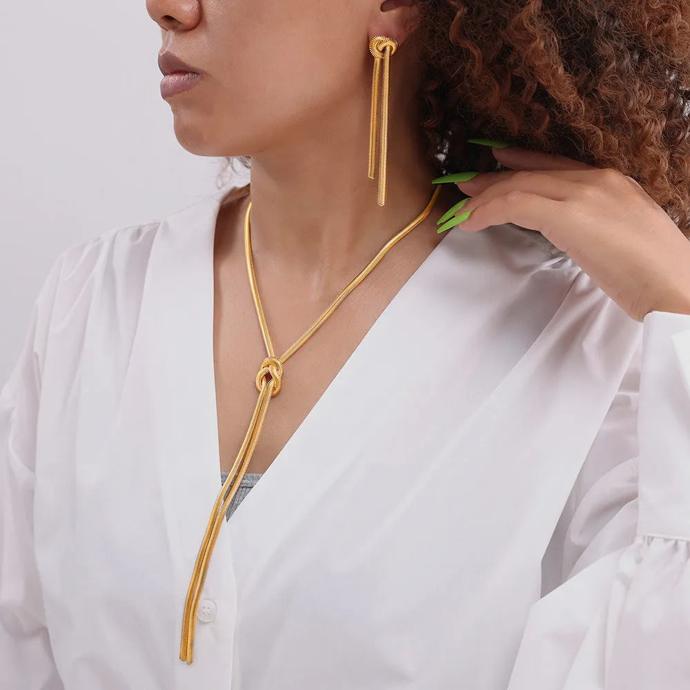 Gold titanium steel necklace with tassel pendant and matching earrings on dark background