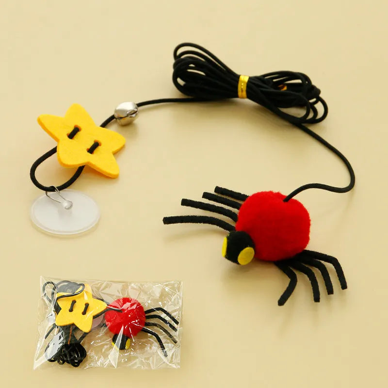 Red and yellow elastic rope cat toy hanging from a door, with feathers, a plastic spider, and a bell.