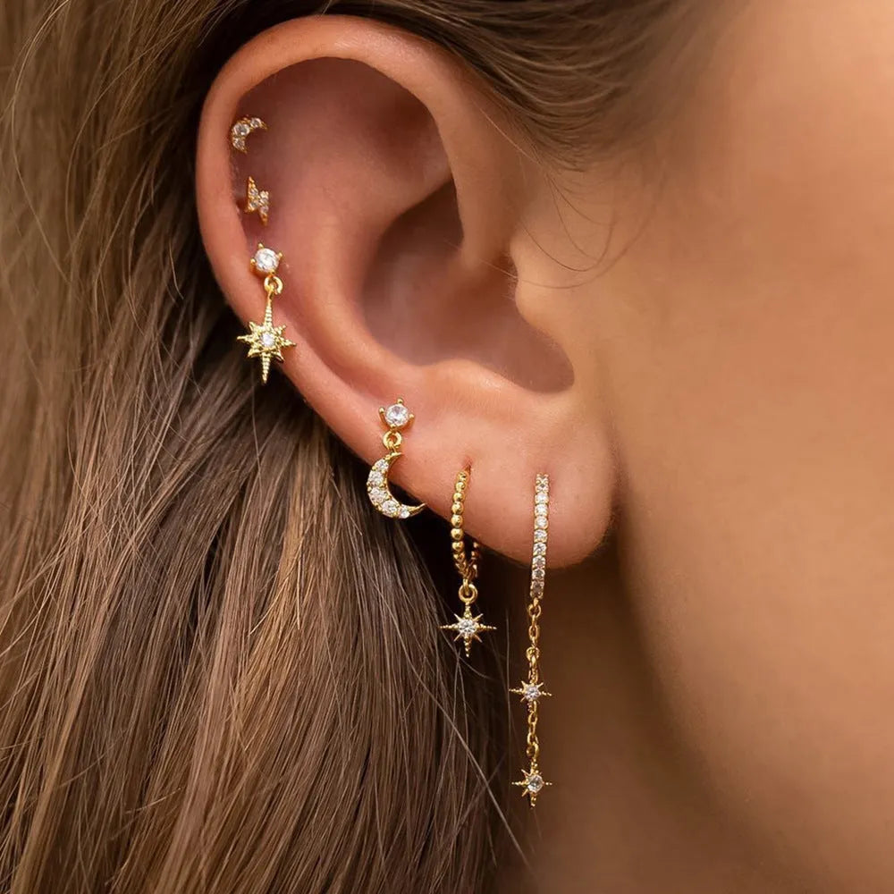 XINGX set of six gold chain tassel and zircon stud drop earrings laid out on a dark surface