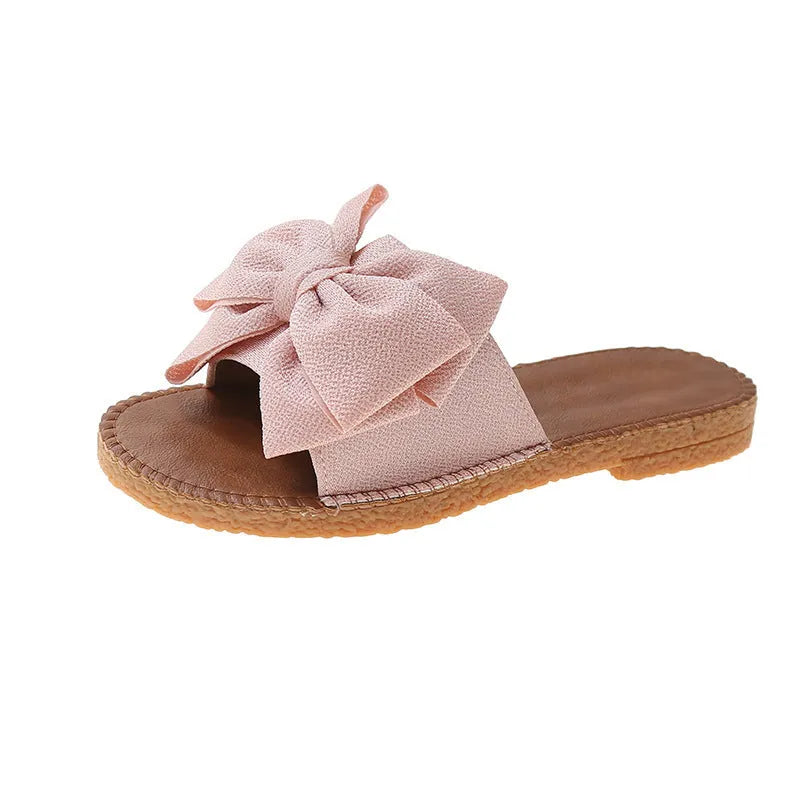 Women's beige suede slip-on sandals with a bow and soft rubber flat sole.