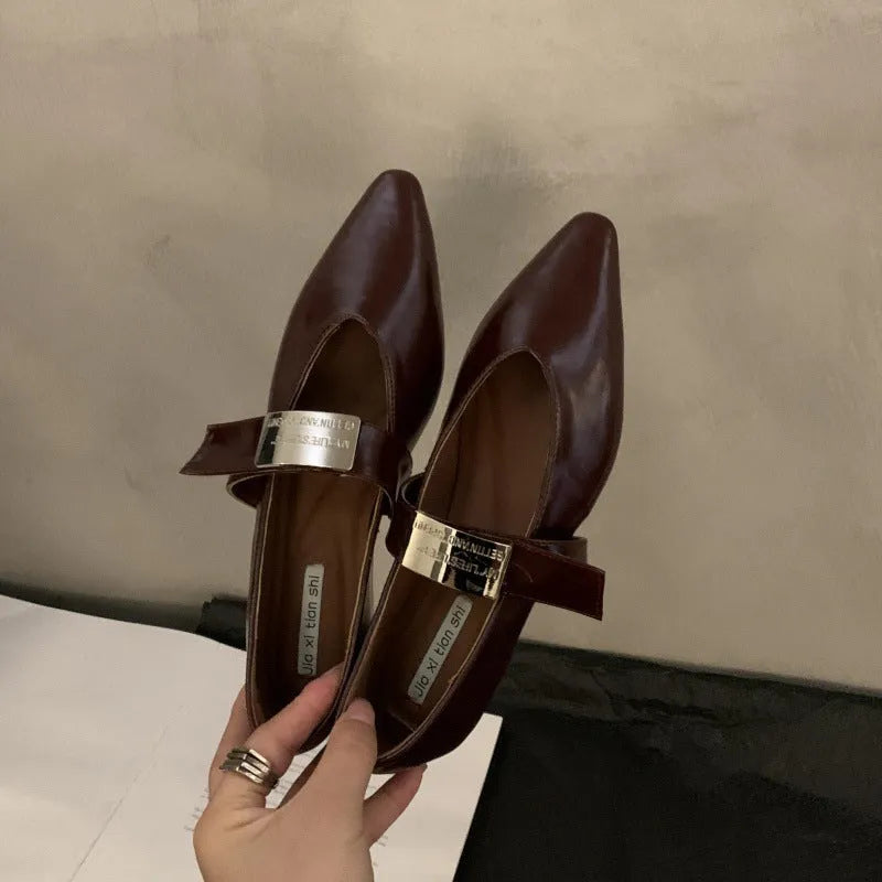 Women's black pointed toe Mary Jane shoes with a silver buckle and a low flat heel.