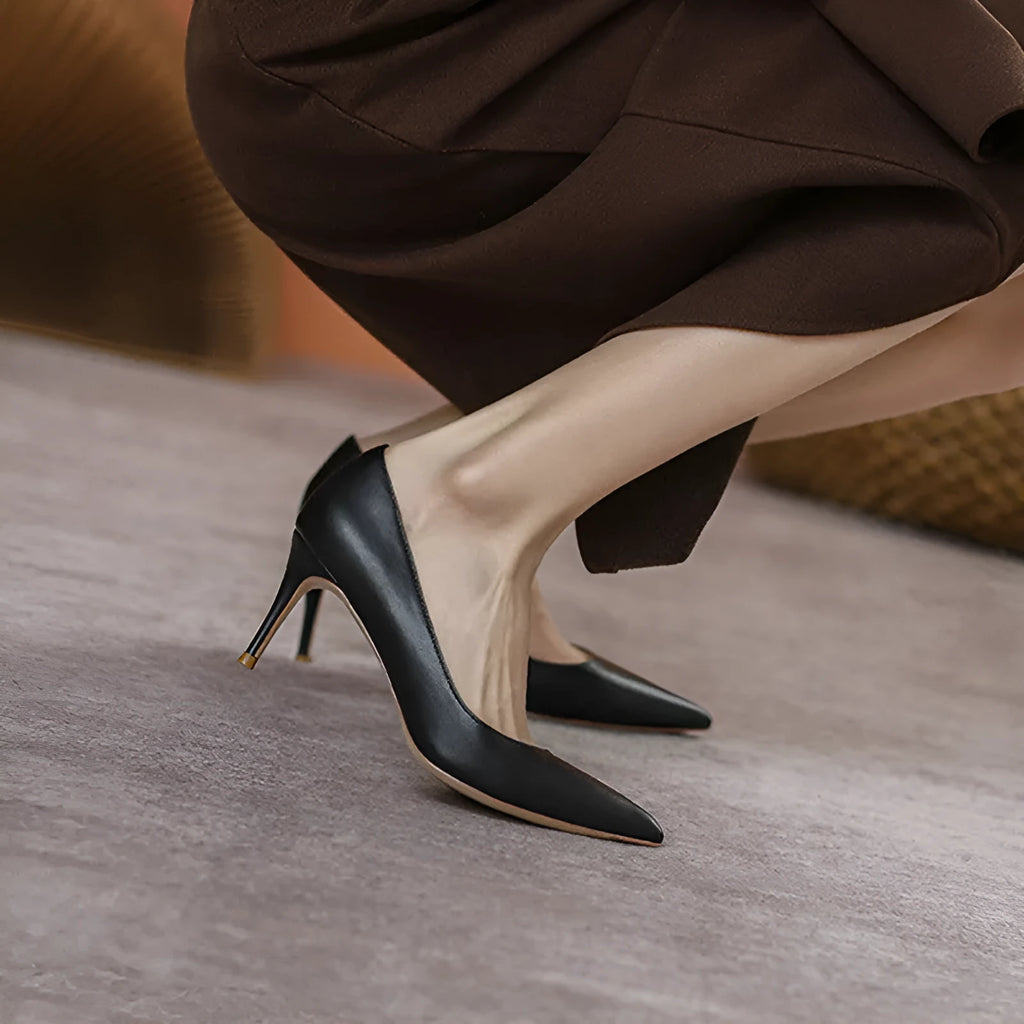 Black pointed-toe high heel shoes with a stiletto heel on a plain background