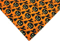 Black and orange reversible Halloween dog bandana with pumpkin and spider web patterns, shown on a dog's neck.