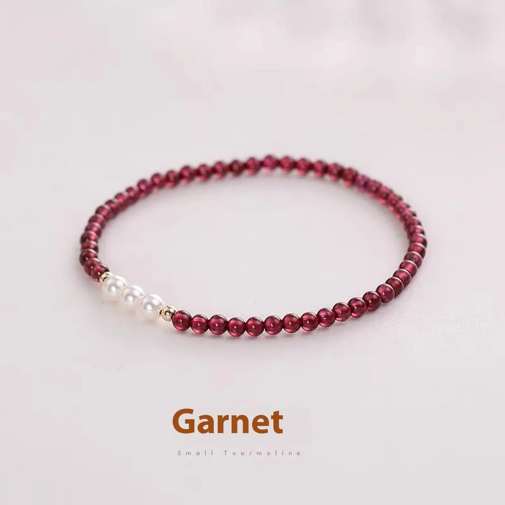 Close-up of a women's adjustable crystal bracelet with red garnet and white artificial pearl beads.