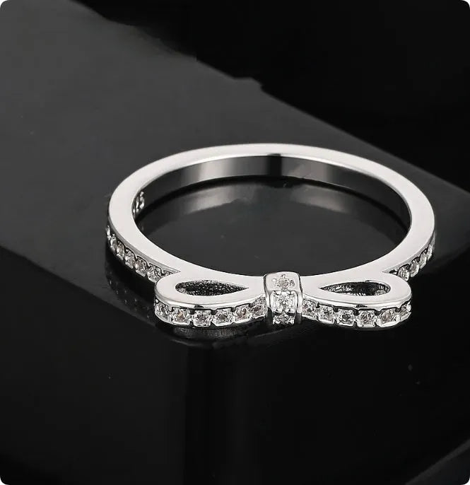 Silver bow-shaped ring with zircon crystal accents on finger, showing electroplated finish and detailed bow structure
