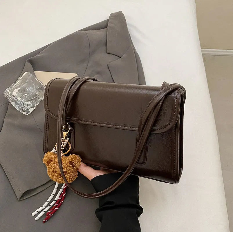 Brown women's structured shoulder bag with horizontal square shape, pendant accessory, and double joint shoulder straps