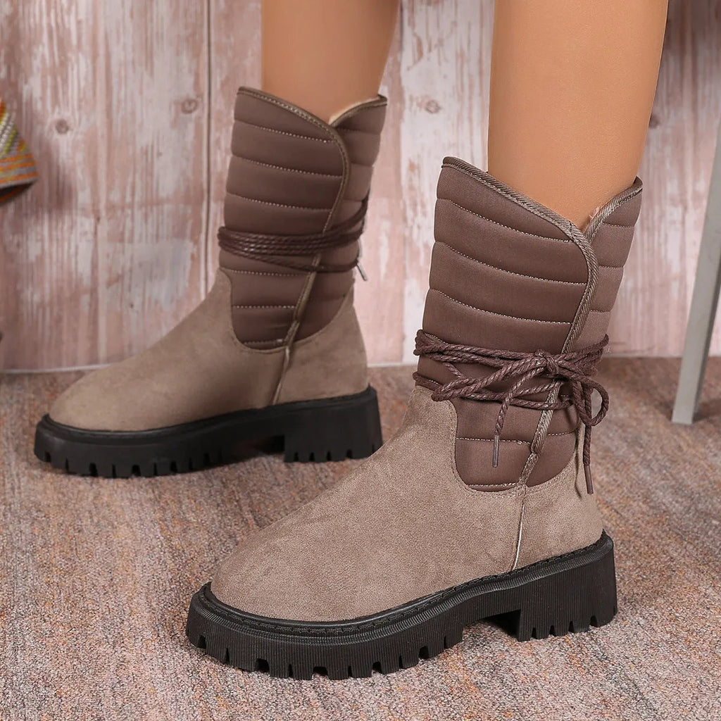 Women's black chunky heel snow boots with suede upper, rubber sole, and lace-up design on wooden floor