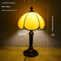Beige fabric bedside lamp with 20cm wide shade on a table.