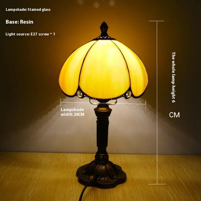Beige fabric bedside lamp with 20cm wide shade on a table.