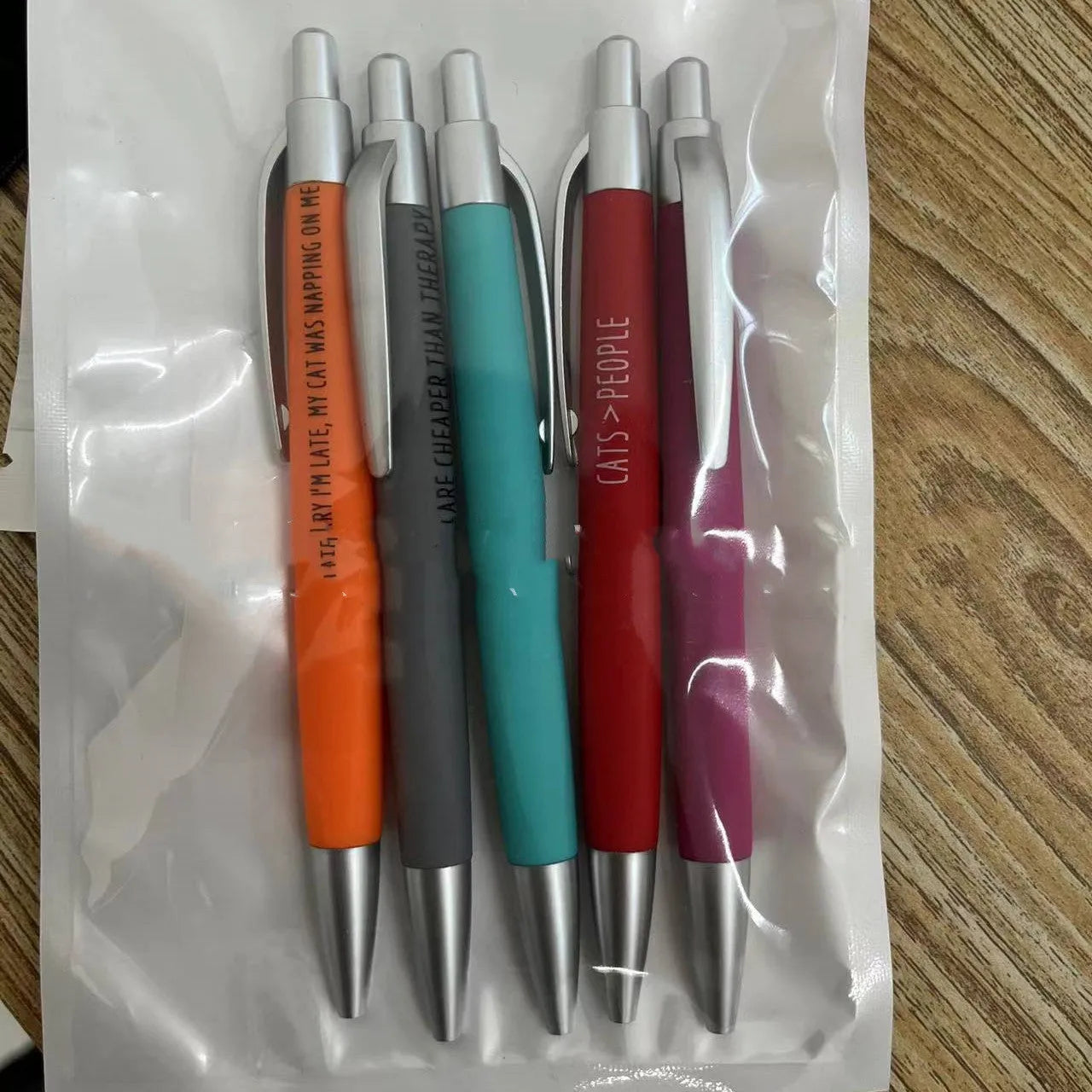 Set of five coloured push-action pens with cat and dog designs next to a beaded storage bag.