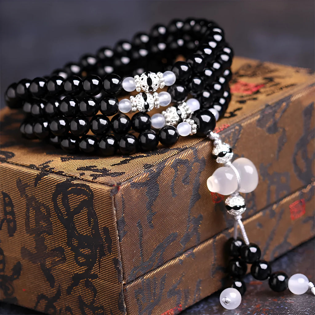 Black agate bracelet with 108 beads and geometric shape on a wrist.