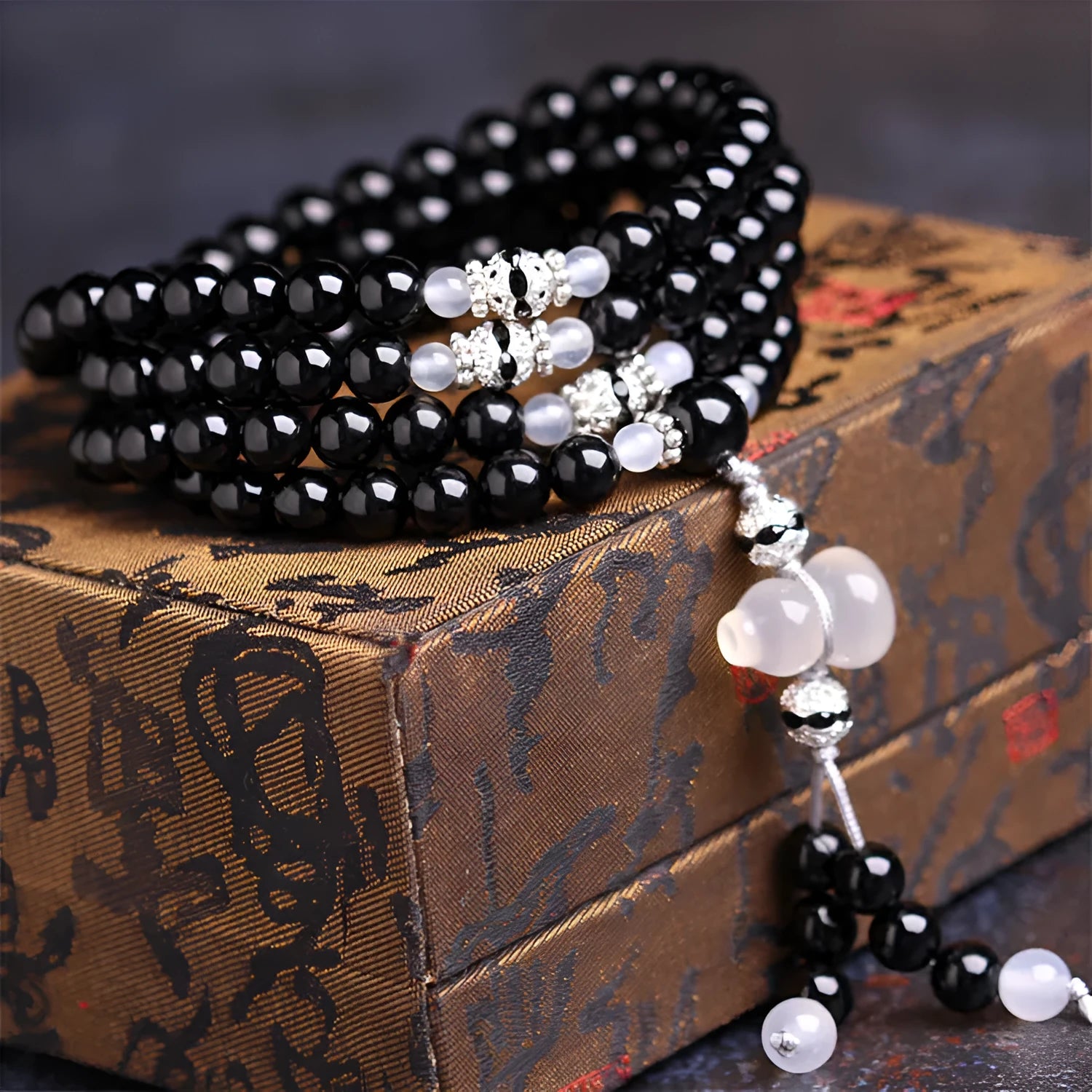 Black agate bracelet with 108 beads and geometric shape on a wrist.