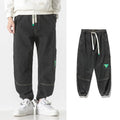 Men's loose-fit tapered trousers in 100% cotton, available in black, blue, and grey colours, showing tapered leg design.