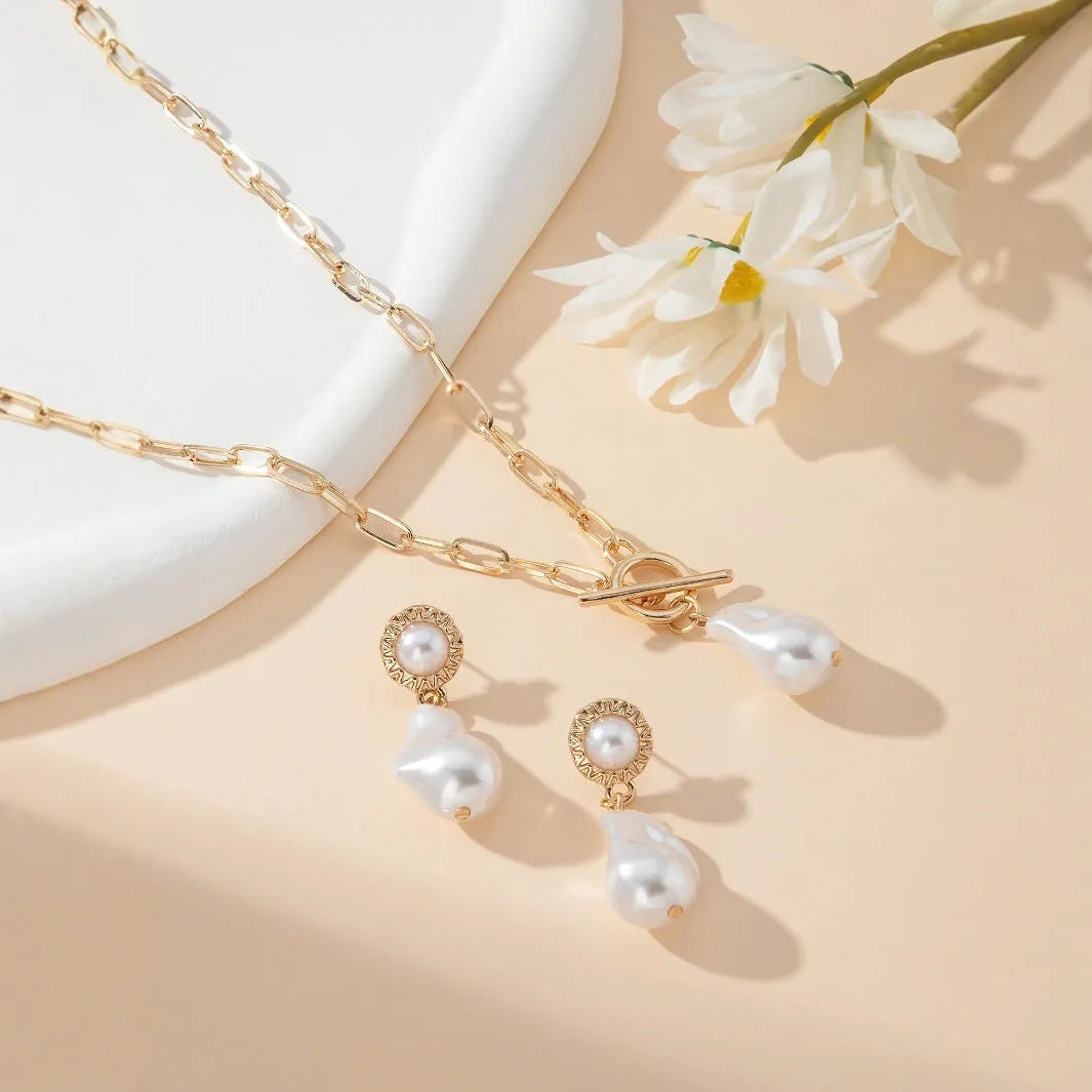 Gold-coloured iron necklace and earrings set with baroque pearl decorative elements on dark background
