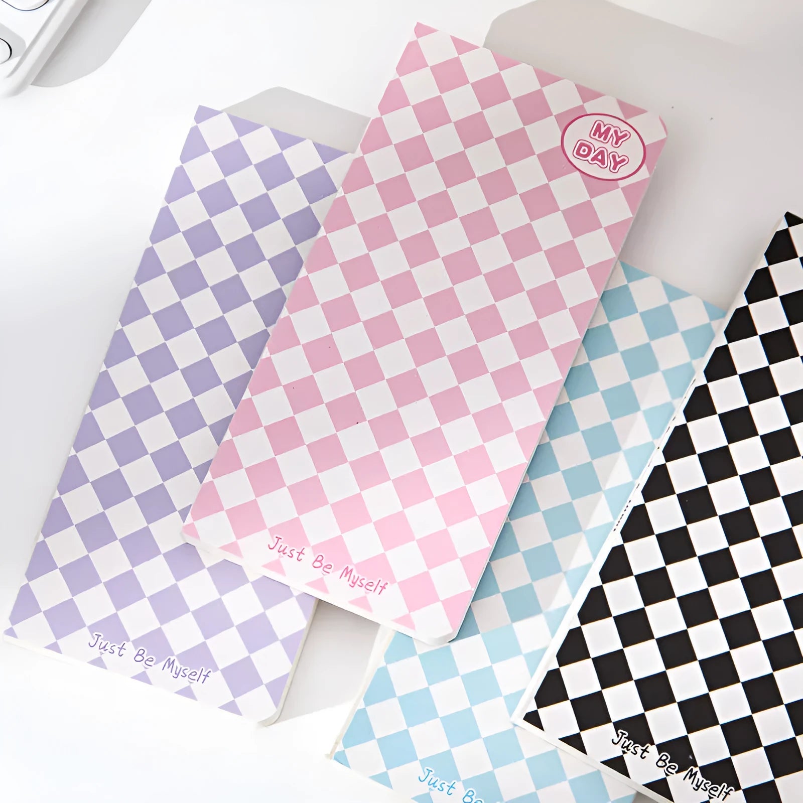 Manual ledger notebook with 100 sheets showing 12 different cover designs including checkerboard and fruit patterns