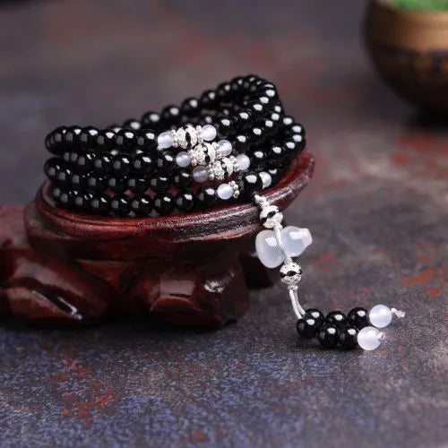 Black agate bracelet with 108 beads and geometric shape on a wrist.