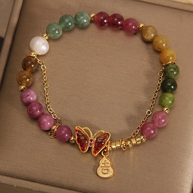 Close-up of a women's agate and tourmaline charm bracelet with butterfly and gourd shapes on a white background.
