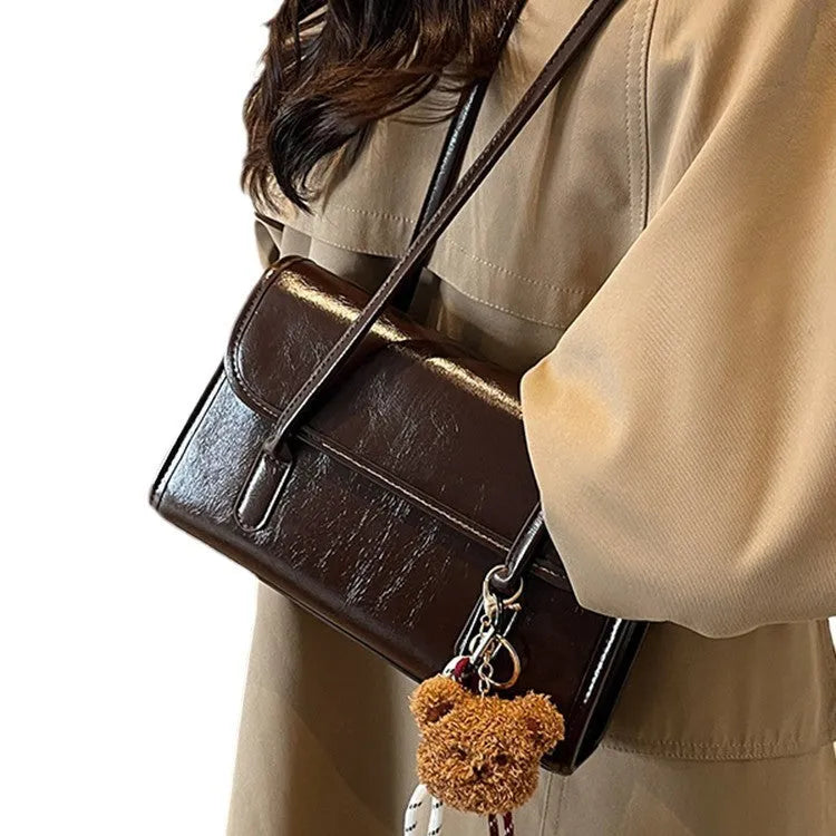 Brown women's structured shoulder bag with horizontal square shape, pendant accessory, and double joint shoulder straps