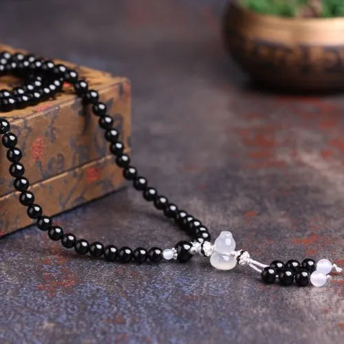 Black agate bracelet with 108 beads and geometric shape on a wrist.