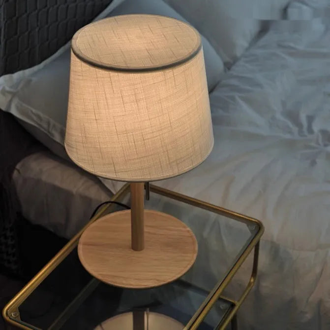 Walnut colour solid wood bedside lamp with a white fabric shade on a wooden surface.