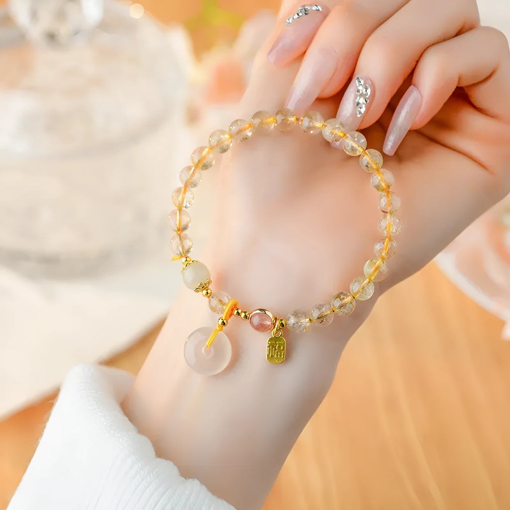 Gold rutilated quartz crystal bracelet with a safety buckle and a small rectangular blessing card pendant.