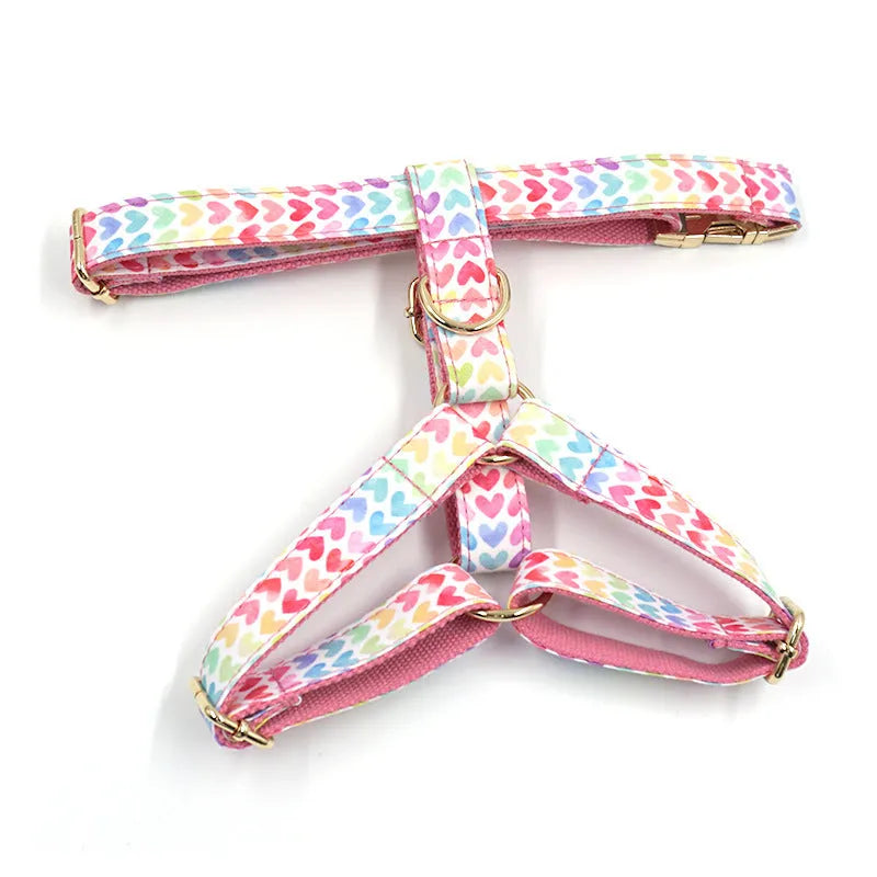 Pink colourful dog harness with heart-shaped stone details and a gold buckle on a white background.
