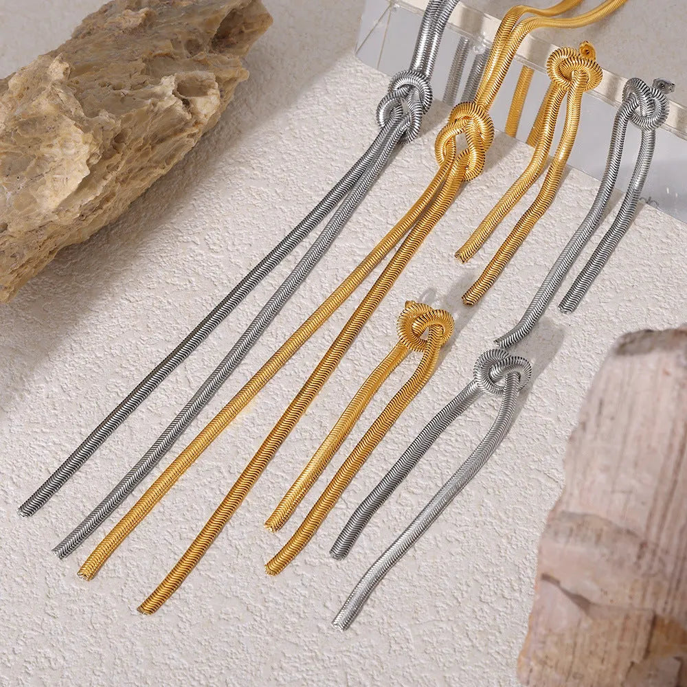 Gold titanium steel necklace with tassel pendant and matching earrings on dark background
