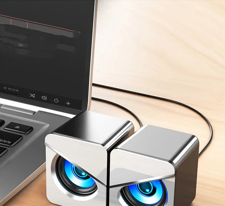 Black and white USB desktop mini speaker with cable next to a laptop computer.