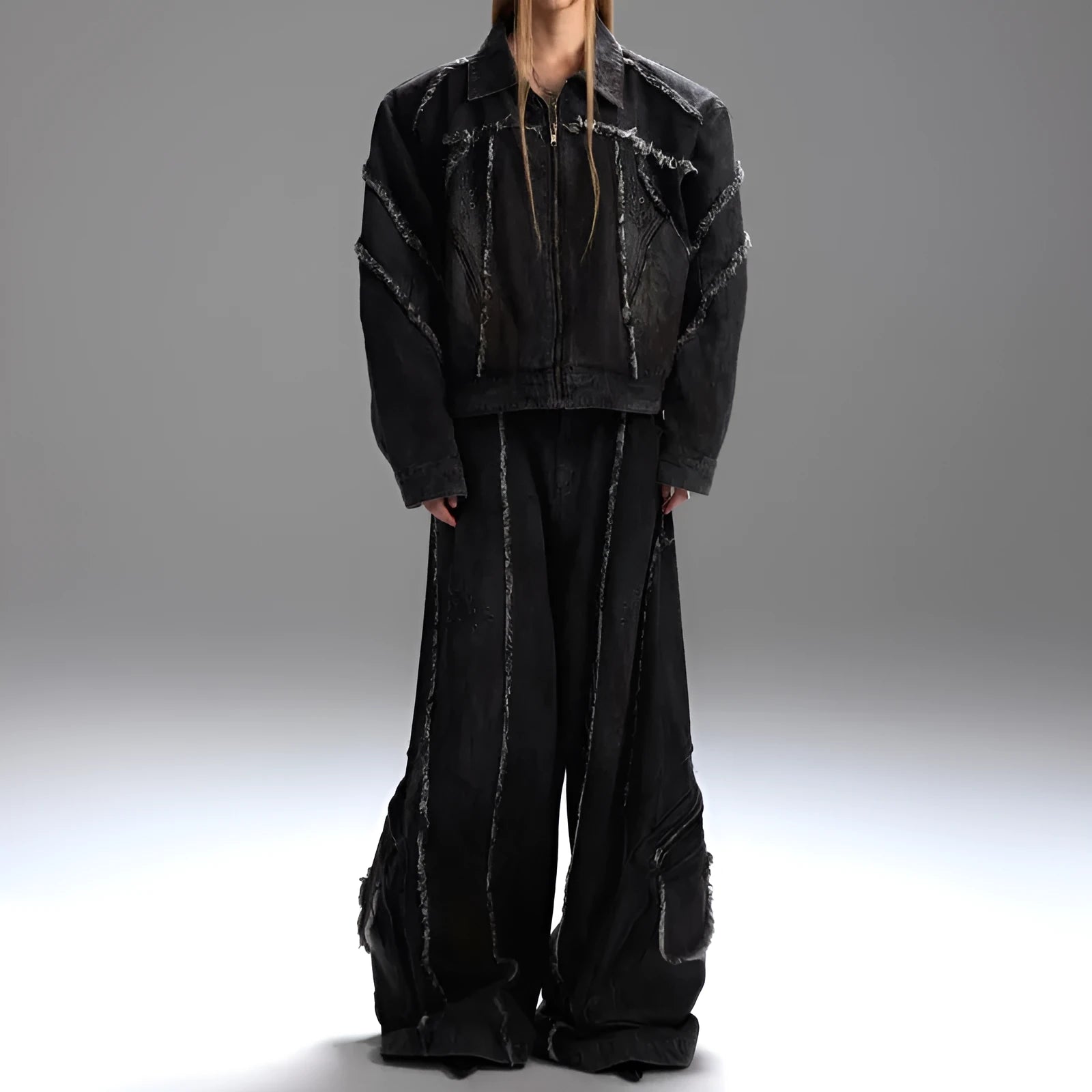 Black gradient denim coat with distressed raw edges and padded shoulders, worn with matching black denim trousers.