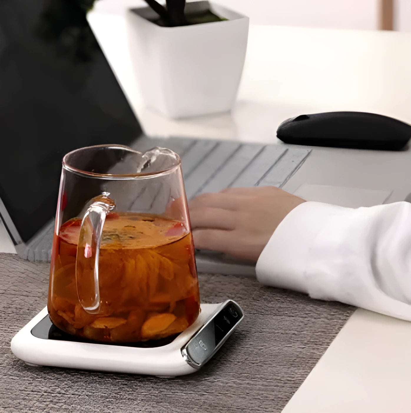 Black USB-powered cup warmer heating coaster with control buttons on a desk next to a coffee mug.