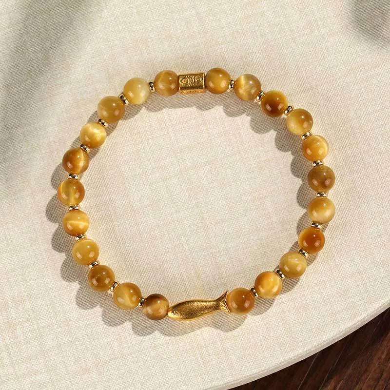 Yellow tiger eye bracelet with small fish bead charm on woman's wrist