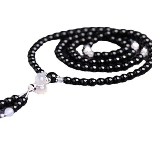 Black agate bracelet with 108 beads and geometric shape on a wrist.