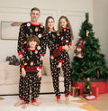 Family wearing matching red plaid Christmas pajamas, including adults, children, and a dog.
