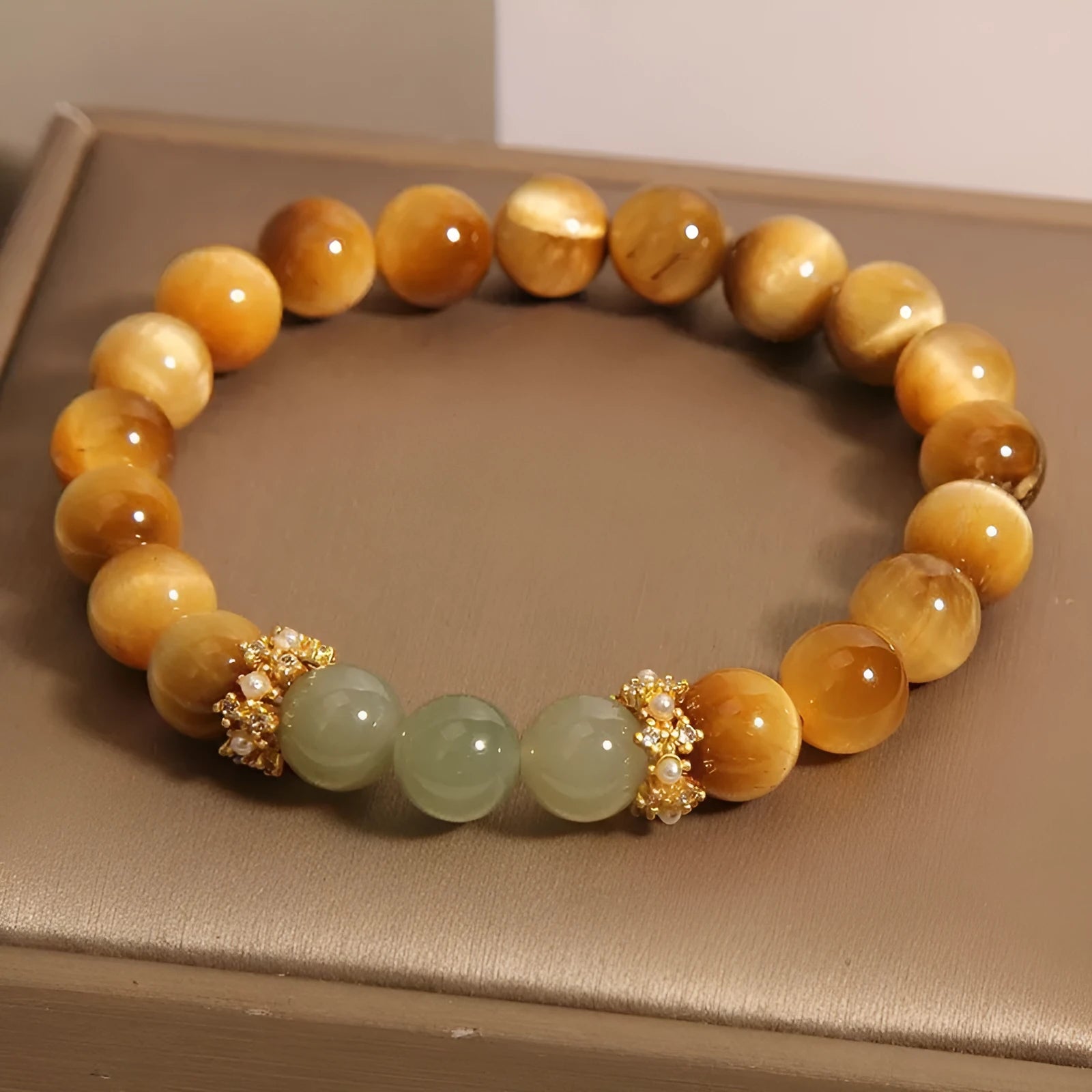 Natural yellow tiger's eye stone bead bracelet with gold gourd charm on a white background.