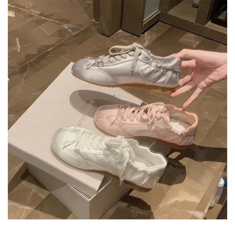 Women's silver grey satin ballet flat with front lace-up fastening and a round toe, shown on a white background.