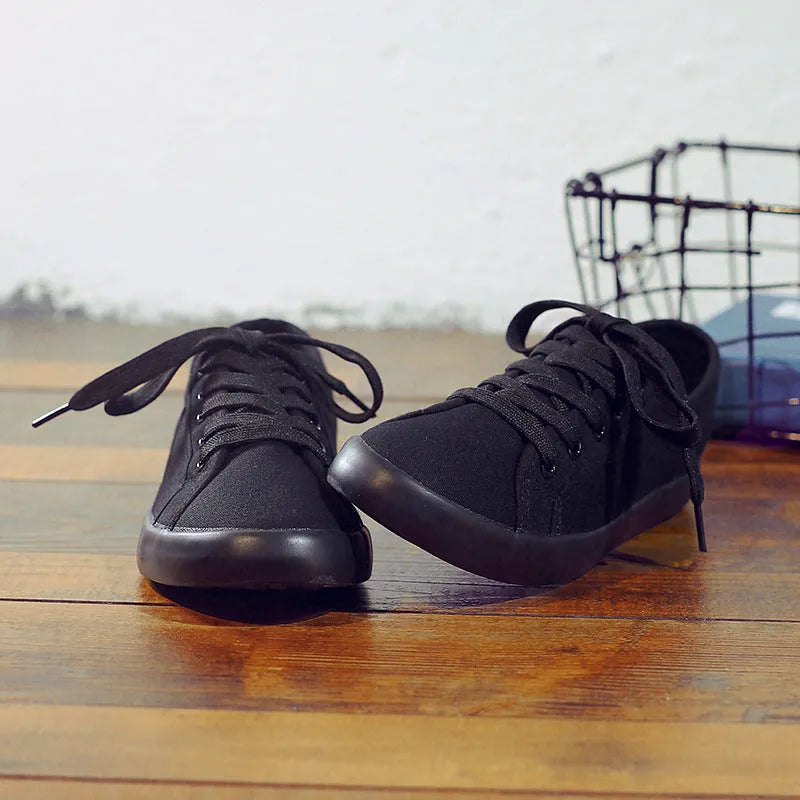 All black low-top canvas lace-up flat shoes for women with a rubber sole.