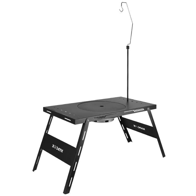 Black folding steel camping table with an integrated barbecue grill set up outdoors.