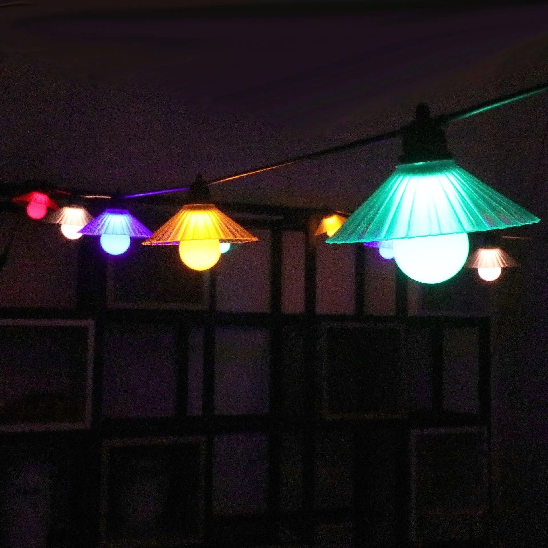 Outdoor LED string lights with white flower-shaped bulbs hanging in a garden setting.