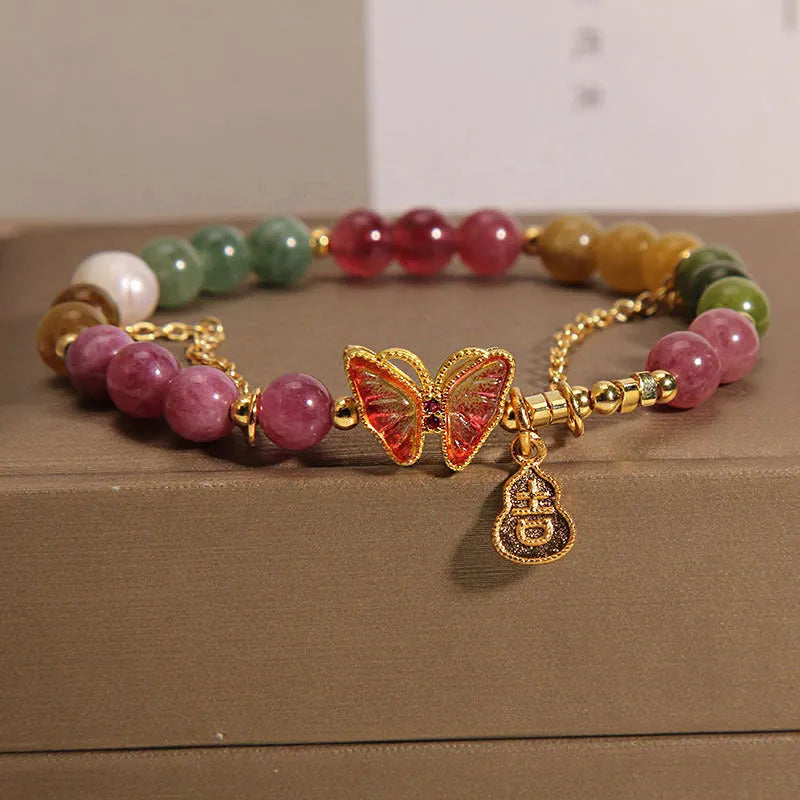 Close-up of a women's agate and tourmaline charm bracelet with butterfly and gourd shapes on a white background.