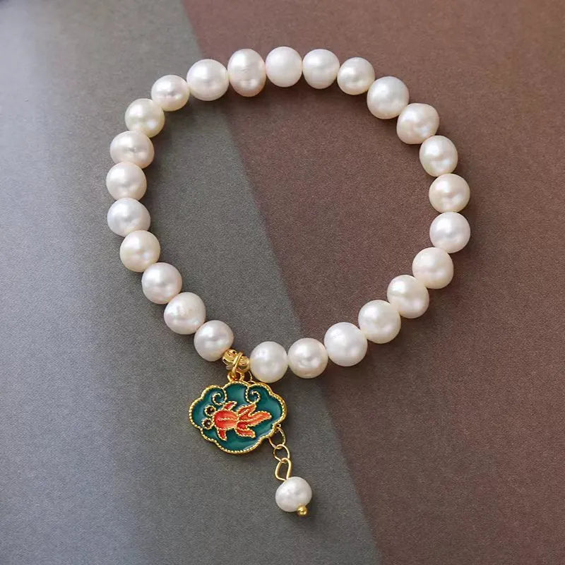 White freshwater pearl and gold electroplated lotus goldfish pendant on an antique style women's bracelet.
