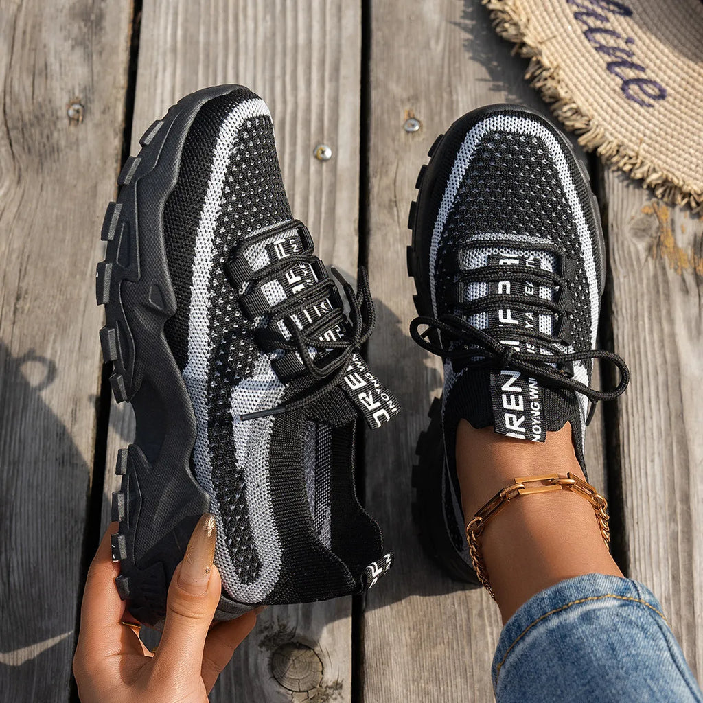Women's Flyknit mesh sneakers in grey and white, showcasing the breathable upper and flat rubber sole.