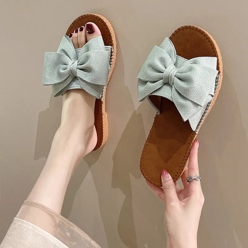 Women's beige suede slip-on sandals with a bow and soft rubber flat sole.
