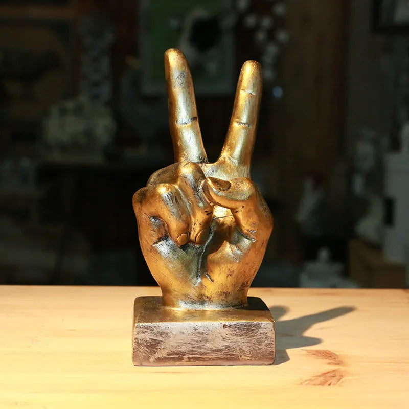 Bronze and silver resin hand gesture ornaments on a wooden desk, showing like, ok, and scissors hand signs.