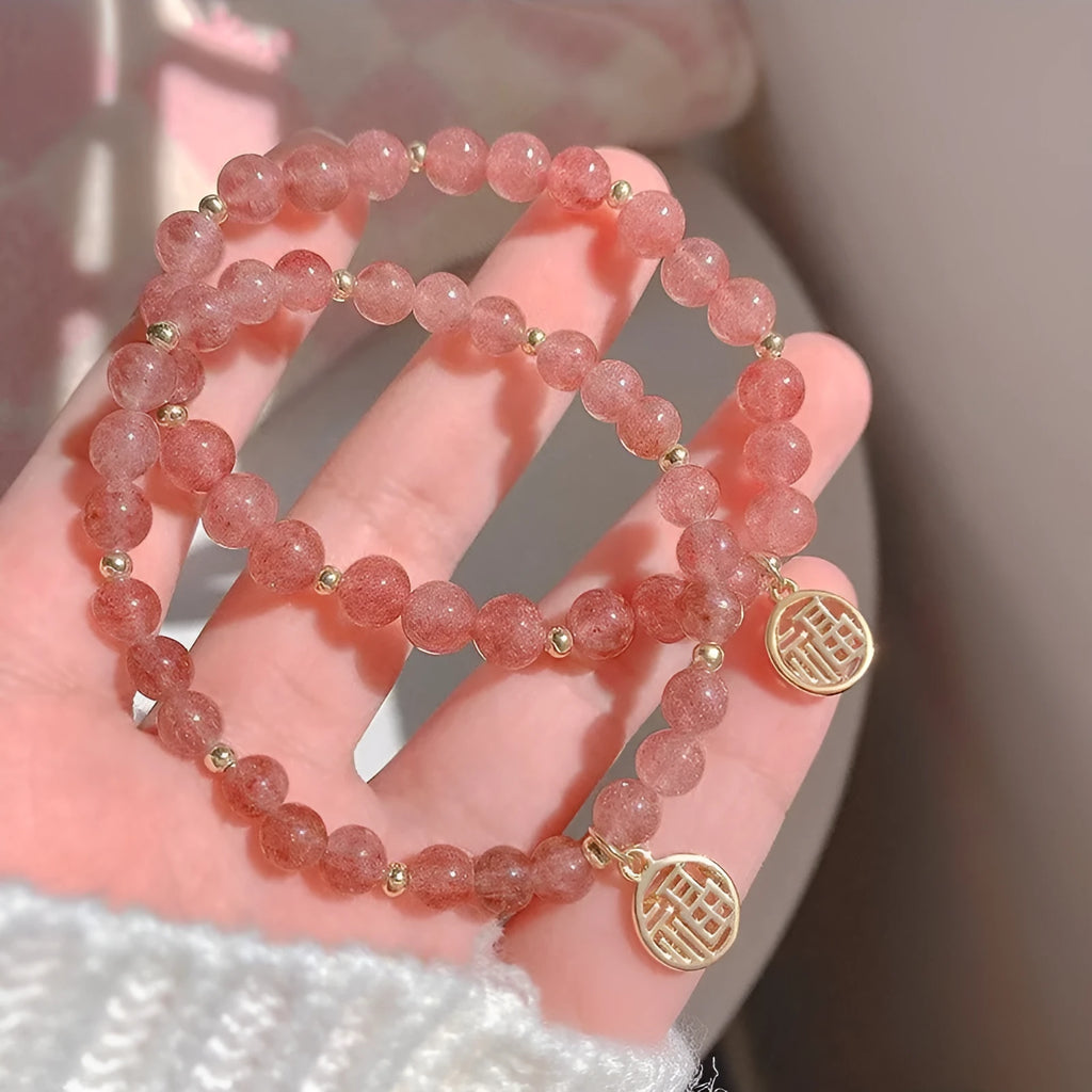Handmade strawberry quartz style glass bead bracelet with a blessing card charm on a wrist.