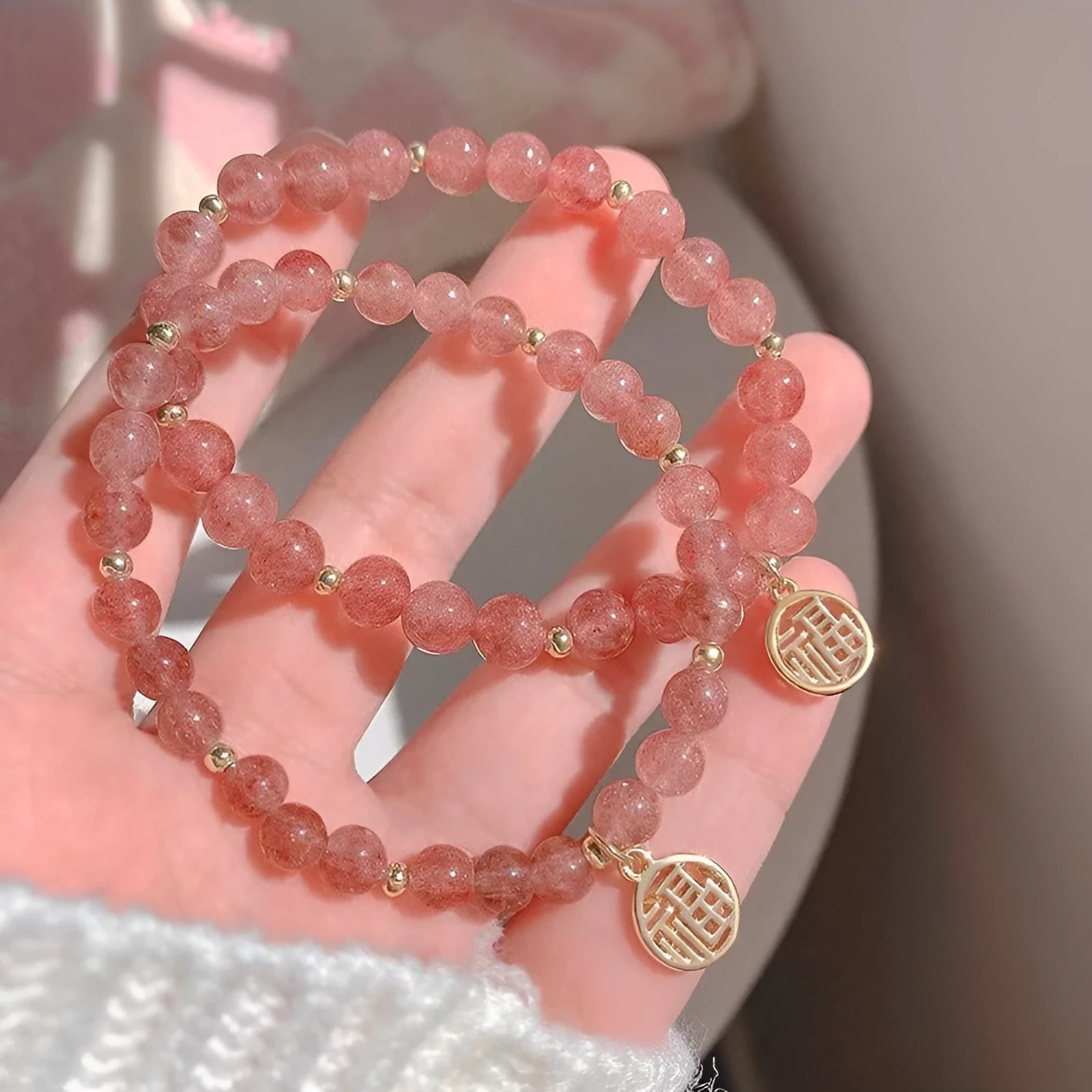 Handmade strawberry quartz style glass bead bracelet with a blessing card charm on a wrist.